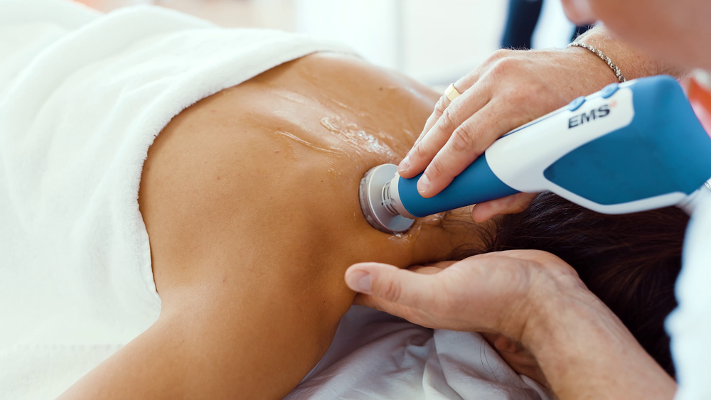 A chiropractor uses shockwave therapy on a patient’s upper back to relieve muscle tension and pain.