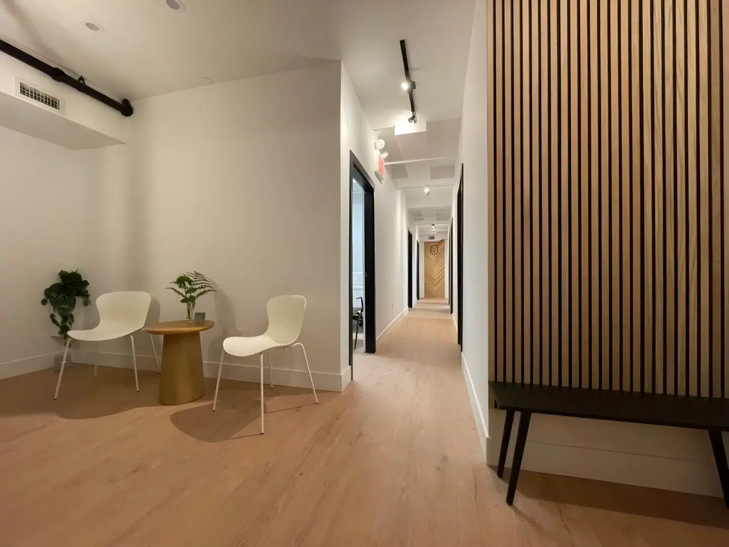 Minimalist waiting area with white chairs, wooden table, and hallway at Brooklyn Chiropractic Care