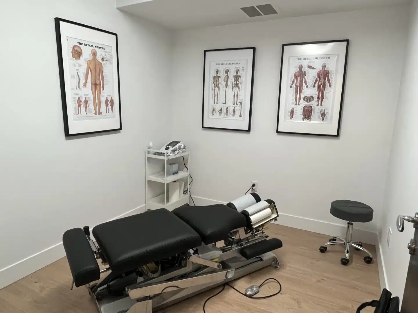 Interior of a private treatment room at Brooklyn Chiropractic Care featuring a chiropractic drop table and anatomical wall charts.